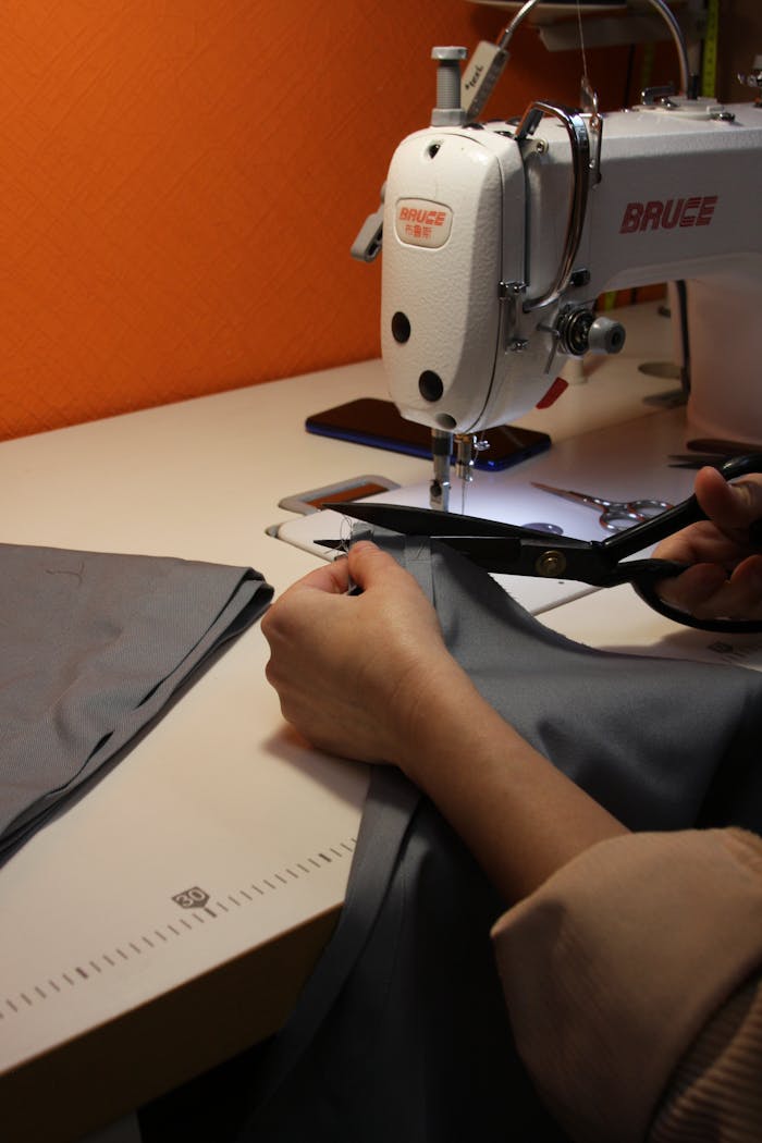 team-02 A person using scissors to cut fabric near a sewing machine, highlighting craftsmanship.