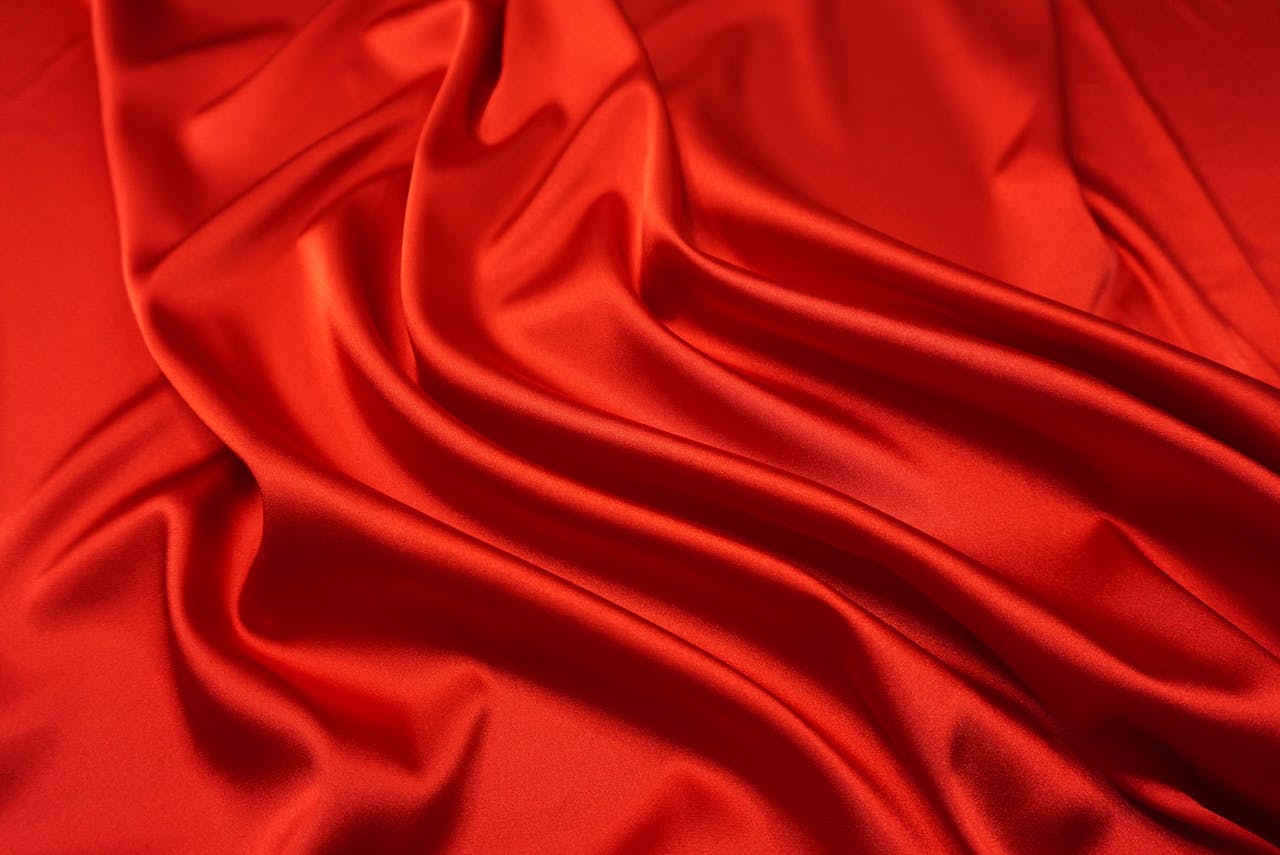team-03 Close-up of smooth, red silk fabric with elegant ripples, highlighting its texture and shine.